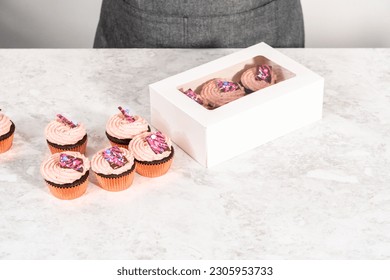 Packaging freshly baked chocolate strawberry cupcakes garnished with gourmet mini pink chocolates into a white paper cupcake box. - Powered by Shutterstock