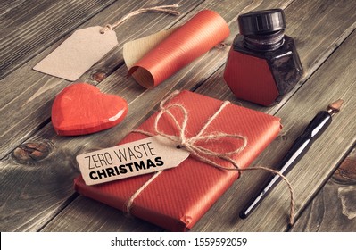  Packed gift box, wrapped in red papertied with cord with text "Zero Waste Christmas" on cardboard tag. Ink, old pen and wrapping paper and red wooden heart on rustic wood. - Powered by Shutterstock