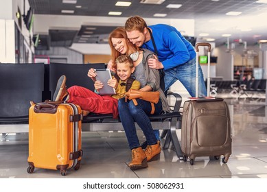 Packed and prepared for take-off. Smiling happy family doing holiday trip and looking map on digital tablet at airport hall