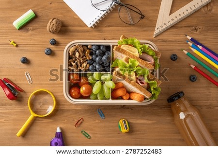 Packed school lunch box with ham and cheese sandwich, grapes, blueberry, cherry tomato, walnut, carrot and juice promoting healthy eating and balanced nutrition at school