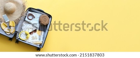 Packed suitcase with belongings on yellow background with space for text