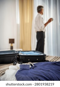 Packed suitcase and clothes while senior businessman enjoys morning coffee before business departure.