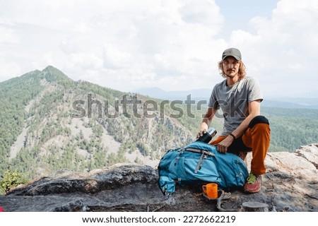 Packing a backpack on a hike, putting equipment in a bag, a camping kit for survival in the forest, a guy climber resting on a mountain, a man trekking a rock. High quality photo