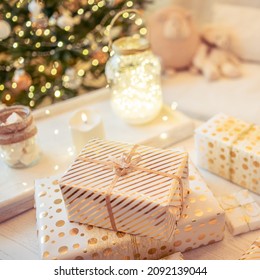 A lot of packing handmade gift boxes lying on the table near Christmas tree in the midst of golden lights, glowing garland, candle. Soft focus. square - Shutterstock ID 2092139044
