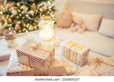 A lot of packing handmade gift boxes lying on the table near Christmas tree in the midst of golden lights, glowing garland, candle. Soft focus - Shutterstock ID 2165605157