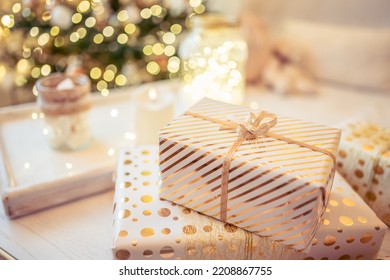 A lot of packing handmade gift boxes lying on the table near Christmas tree in the midst of golden lights, glowing garland, candle. Soft focus - Shutterstock ID 2208867755