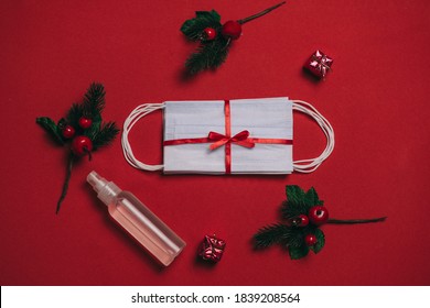 Packing of white medical surgical masks, Christmas present under the Christmas tree on a red background and sanitizer. Coronavirus pandemic, quarantine, 2020, 2021. Celebrating the new year, stay home - Powered by Shutterstock