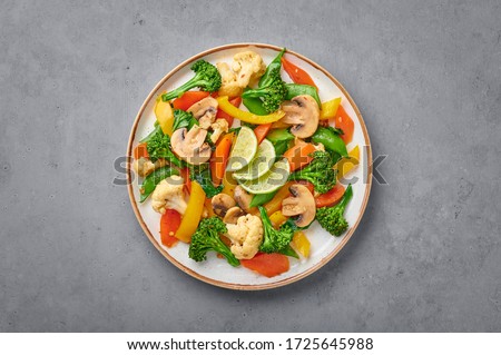 Pad Pak Ruam or Veg Thai Stir-Fried Vegetables in white plate on gray concrete backdrop. Pad Pak is thailand cuisine vegetarian dish with mix of vegetables and sauces. Thai Food. Copy space. Top view
