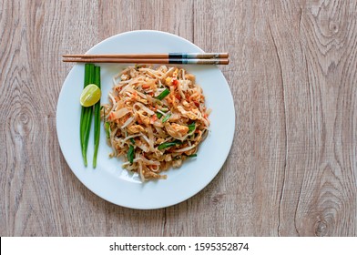 Pad Thai Or Authentic Thai Fried Noodle Serves With Spring Onion And Lime On Round Ceramic White Plate With Chopsticks On Wooden Table Background Aerial Shot From Top View Or Above Or Overhead