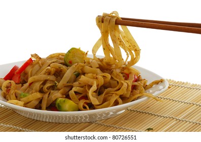 Pad Thai dish on straw pad with chopsticks isolated on white background