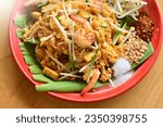 Pad Thai is placed on a brown wooden table. There is a woman squeezing lime juice to add more seasoning. Because Thai people like to eat spicy food. Famous Thai food concept. Street food. Thai identit
