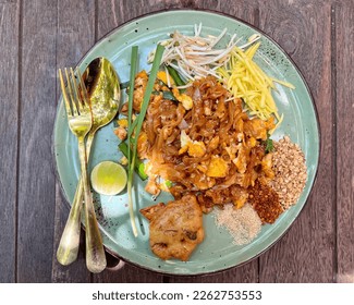 Pad Thai - stir-fried noodles mixed with shrimp, egg, tofu and sour sauce serve with bean sprout, raw mango, lime, sugar, chili, and ground beans on wooden table, Famous Thailand food. - Shutterstock ID 2262753553