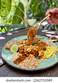 Pad Thai - stir-fried noodles mixed with shrimp, egg, tofu and sour sauce serve with bean sprout, raw mango, lime, sugar, chili, and ground beans on wooden table, Famous Thailand food. - Shutterstock ID 2262753589