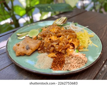 Pad Thai - stir-fried noodles mixed with shrimp, egg, tofu and sour sauce serve with bean sprout, raw mango, lime, sugar, chili, and ground beans on wooden table, Famous Thailand food. - Shutterstock ID 2262753683