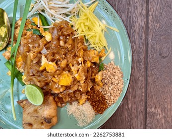 Pad Thai - stir-fried noodles mixed with shrimp, egg, tofu and sour sauce serve with bean sprout, raw mango, lime, sugar, chili, and ground beans on wooden table, Famous Thailand food. - Shutterstock ID 2262753881