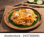 Pad Thai-Stir fried rice noodles with shrimp and sauce in plate on wooden table background. Thai street food