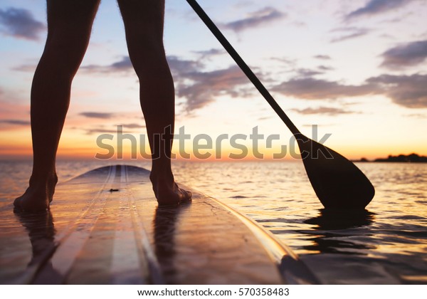 paddle board on the beach, close up of standing\
legs and paddle