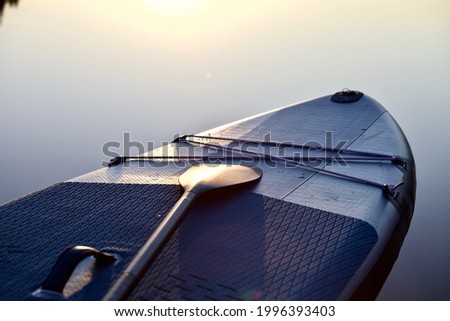 Paddle board and surf board with paddle on blue water surface background close up. Surfing and SUP boarding equipment in sunset lights close-up. Outdoor water sports. Surfing lifestyle backgrounds.