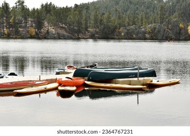 Paddle board and upside down canoes floating on a peaceful  lake in fall with pine covered hill in background and gray sky
