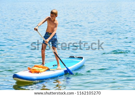 Paddle boarder. Child boy paddling on stand up paddleboard. Healthy lifestyle. Water sport, SUP surfing tour in adventure camp on active family summer beach vacation.
