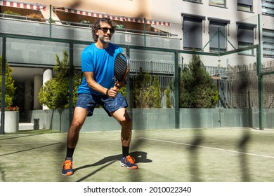 paddle tennis player with beard and sunglasses teaching on a residential paddle court, side view, throw the net - Powered by Shutterstock