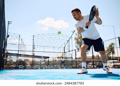 Paddle tennis player hitting the ball while playing match on outdoor court. Copy space. - Powered by Shutterstock