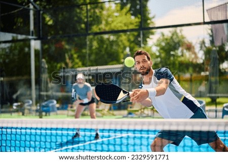 Paddle tennis player hitting the ball during mixed doubles match on outdoor court.
