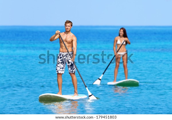Paddleboard beach people on stand up paddle board\
surfboard surfing in ocean sea on Big Island, Hawaii Beautiful\
young multi-ethnic couple, mixed race Asian woman and Caucasian man\
doing water sport.