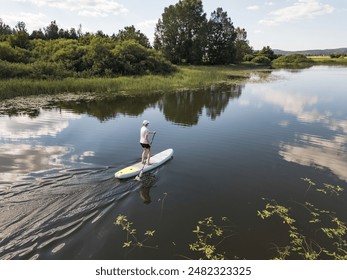 Paddleboarder paddling a sup board on a beautiful calm mountain lake at summer sunset, aerial view. Nature and healthy lifestyles concepts. - Powered by Shutterstock