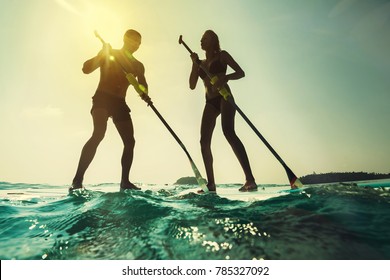 Paddleboarding at sunset. Young couple in the sea with paddle and board. 