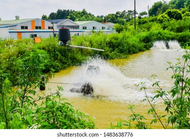 Paddle-wheels Being Used To Aerate Pond In Front Of Buildings In Rural Industrial Park. Water Is Blurry Due To Motion.