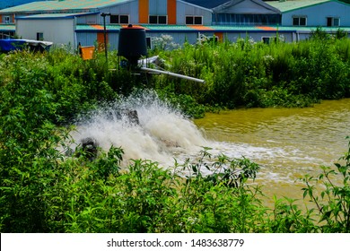 Paddle-wheels Being Used To Aerate Pond In Front Of Buildings In Rural Industrial Park. Water Is Blurry Due To Motion.