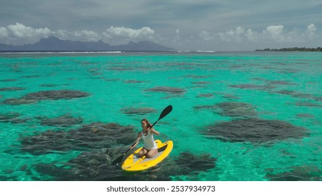 Paddling peacefully in her canoe. A woman explores turquoise waters near a tropical island on a sunny day. With clear skies. Fluffy clouds. And majestic mountains in the distance - Powered by Shutterstock