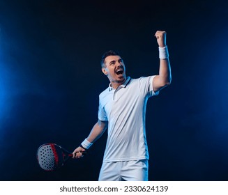 Padel tennis tour player in white sportswear. Man athlete with paddle tenis racket on black background celebrating a set win. Sport concept. Download a high quality photo for sports website. - Powered by Shutterstock