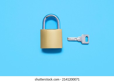 Padlock with a key on a blue background, top view. A gold-colored lock with a silver key on a uniform blue background. The concept of protection and security in the form of a lock and key