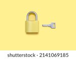 Padlock with a key on a yellow background top view. A golden color lock with a silver key on a plain yellow background. The concept of protection and security in the form of a lock
