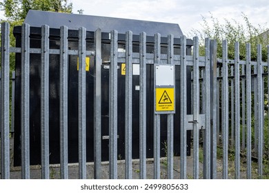 Padlocked gate to black suburban electricity substation with galvanized metal fence, hedge, and danger keep out signs - Powered by Shutterstock