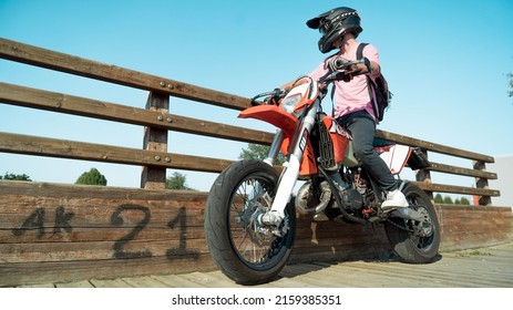 PADOVA, ITALY - Feb 04, 2019: A low angle of a motorcyclist sitting on an orange bike, wearing a helmet against a wooden fence