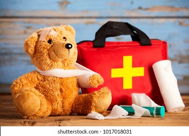 Paediatric healthcare concept with a little teddy bear with its arm in a sling alongside a first aid kit and bandages on rustic wood