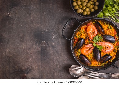 Paella background, space for text. Paella in black pan with saffron rice, peas, shrimps, mussels, squid, meat. Seafood paella, traditional spanish dish. Paella on rustic black wooden table. Top view