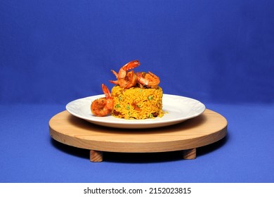 Paella Rice Is A Traditional Cuisine Recipe From The City Of Valencia Spain Prepared With Saffron, Seafood, Shrimp, Vegetables Served On A White Plate On A Blue Background