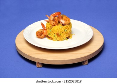 Paella Rice Is A Traditional Cuisine Recipe From The City Of Valencia Spain Prepared With Saffron, Seafood, Shrimp, Vegetables Served On A White Plate On A Blue Background