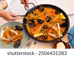 Paella with seafood - traditional Spanish dish. Female hands serving paella on plates at a festive table