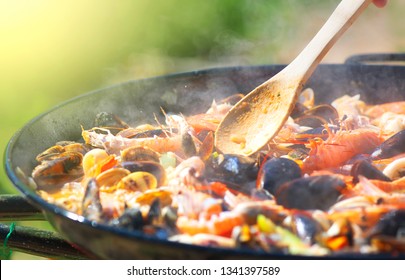 Paella traditional Spanish food, seafood paella in the fry pan with mussels, king prawns, langoustine and squids. Cooking paella outside, closeup