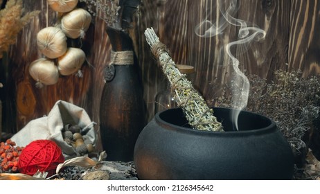 Pagan Witch Magic Altar. Smoking Twist Of Bitter Wormwood Herb For Fumigation In Cast Iron Cauldron, Ritual Objects In Wooden Background, Dark Key, Selective Focus.