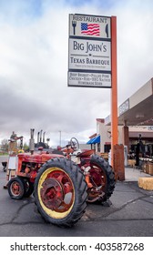 PAGE, ARIZONA- Mar 30, 2016: Texas Barbeque Restaurant Exterior. Big Sign With American Flag Advertises Bbq Beef Brisket, Pulled Pork, Ribs. Outdoor Seating With Bales Of Hay, Vintage Tractor