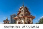 The pagoda of an ancient Burmese Buddhist Temple against the blue sky. The roof has triangular cornices and a golden spire. Decorative carvings, patterns, columns.A skyscraper in the distance.Malaysia