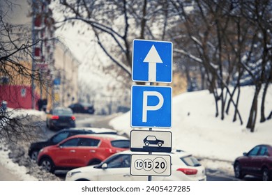 Paid parking lots in downtown, park sign on pole in winter day. Row of cars parked on snowy roadside in winter, paid parking sign. Winter parking problems. 
