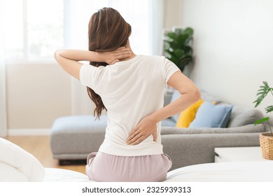 Pain body muscles stiff problem, asian young woman painful back, neck ache from work hand holding massaging rubbing shoulder hurt, sore sitting on bed while wake up at home. Health care and medicine. - Shutterstock ID 2325939313
