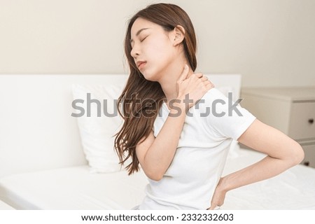 Pain body muscles stiff problem, asian young woman painful with back, neck ache from work hand holding massaging rubbing shoulder hurt, sore sitting on bed in room at home. Health care and medicine.